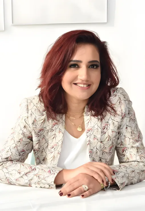 Professional portrait of Shraddha Barot Amariei, CEO of White Window Real Estate, smiling and wearing a patterned blazer in a bright, modern office setting.