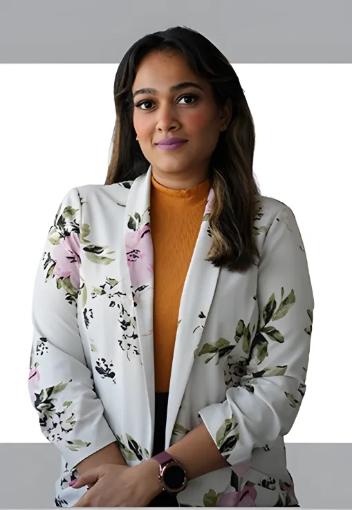 Professional headshot of Shruti Krishnan, Sales Manager of White Window Real Estate, wearing a floral white blazer and mustard top against a clean studio background.